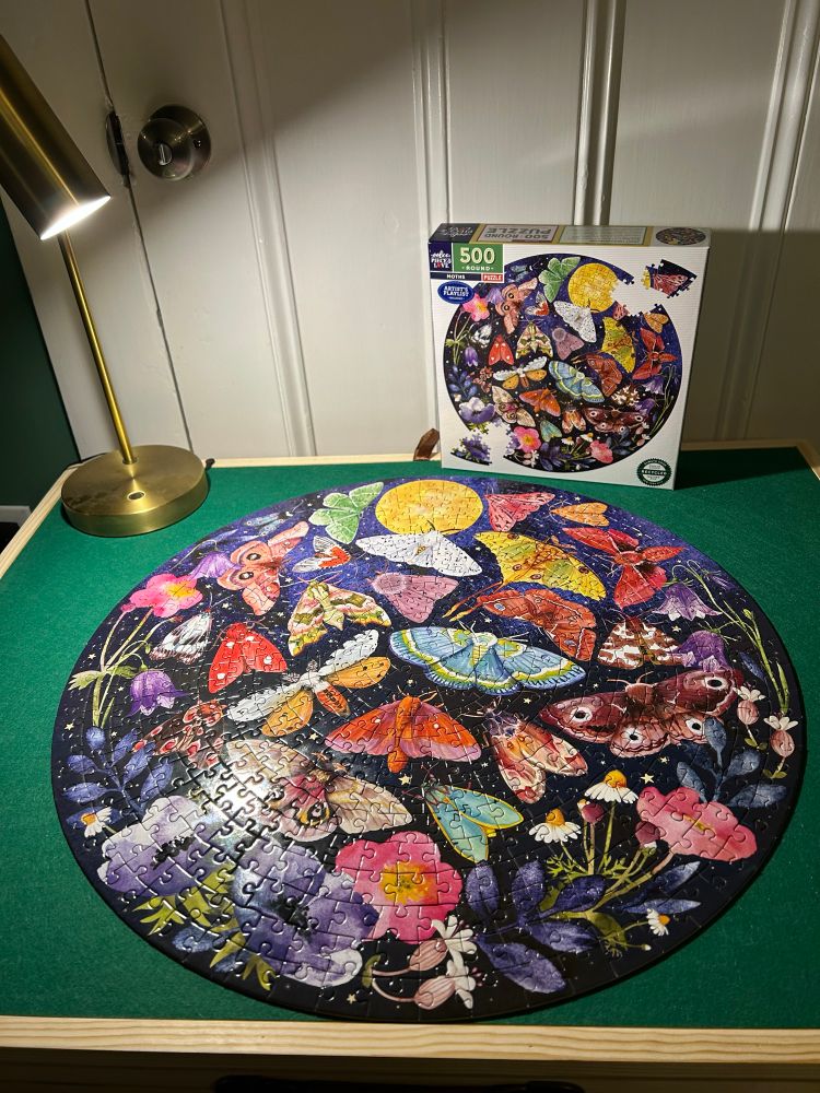 Image shows a round puzzle depicting moths and flora on a puzzle table.
