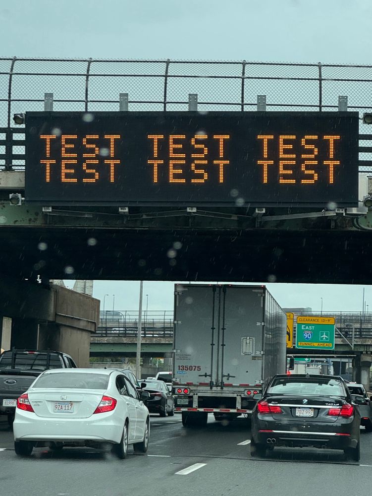 I-95 with traffic in the rain. An electronic road sign on a bridge says TEST TEST TEST TEST TEST TEST