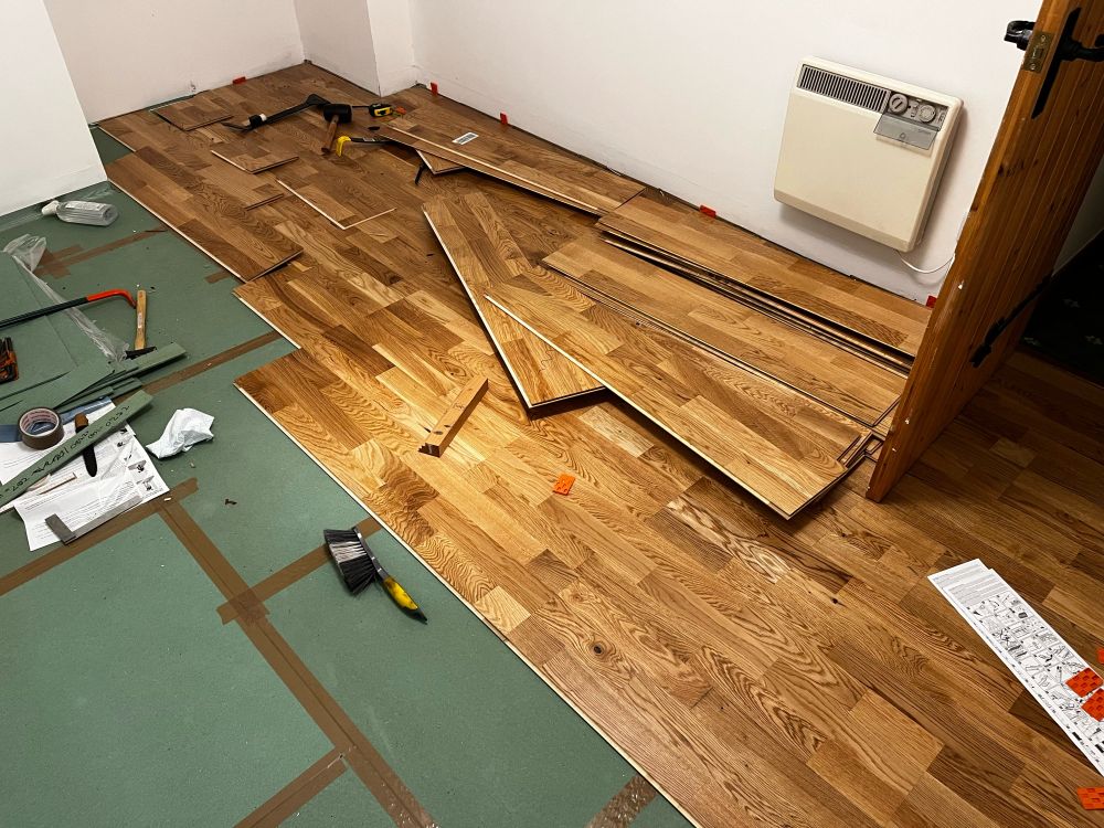 a room half floored, half underlay, tools and offcuts of wood spread everywhere