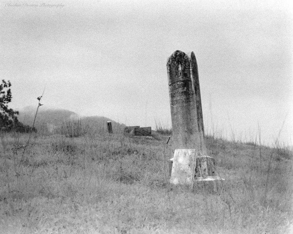 Black and white film photo of the historic Dix Hill Cemetery in Waynesville, North Carolina. This was captured on expired Svema 64 film produced in the Soviet Union. I did some bracketing to determine that +3 stops (8 ISO) was the minimum baseline for usable shots. I could probably shoot at 4 or even 2 ISO. I stand developed for 1hr in Rodinal 1+100 dilution.  The base fog was intense and there was a lot of grime on the shots but I still managed to pull a few usable, albeit grungy looking shots from the roll.