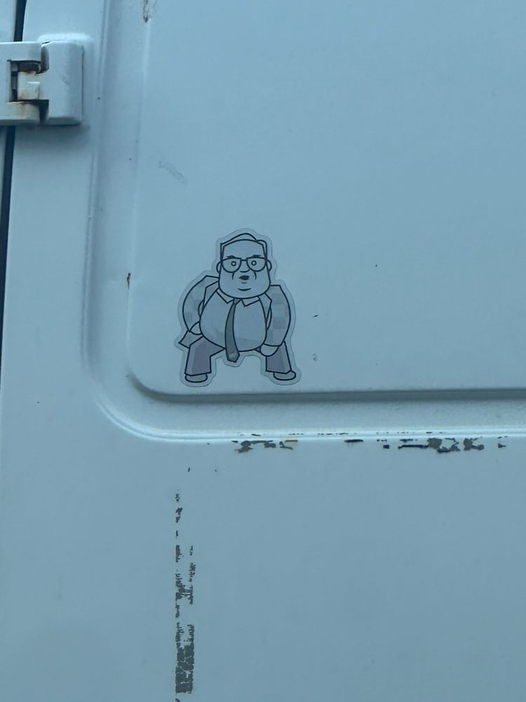 A picture of a sticker on a dirty white van. The sticker is a cartoonish depiction of Chris Farley as Matt Foley from Saturday Night Live, who lives in a VAN DOWN BY THE RIVER!!! 
