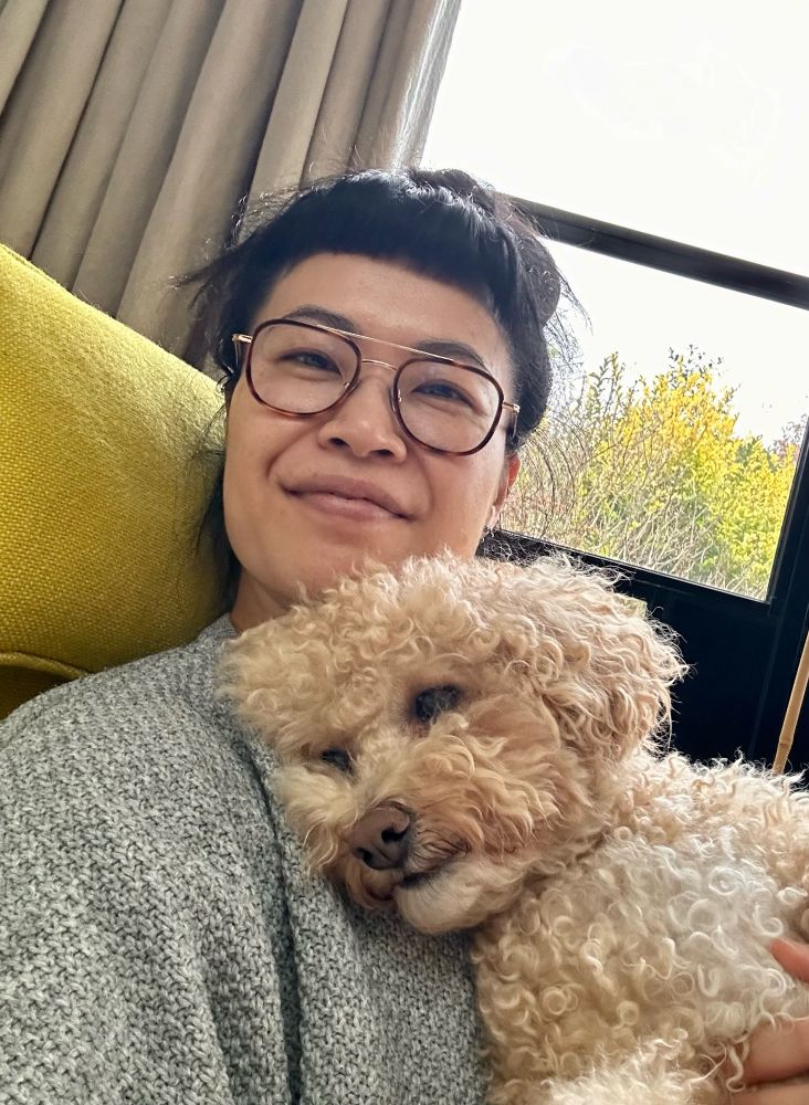 Female with glasses on holding a fluffy dog sitting in a yellow chair