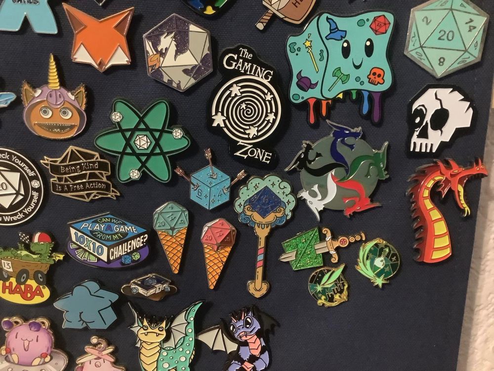This section of pin banner shows pins focused more on RPGs like a gelatinous cube with a rainbow of colored objects inside, a wand with a 8 sided die on top of it and a 20 sided die with the phrase being kind is a free action.