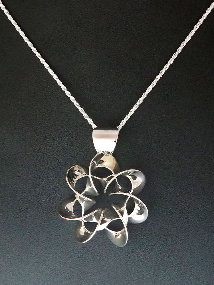 Photograph of a flower-like mirror-polished sterling silver pendant, about 1.2in/30mm across, with seven-fold rotational symmetry. 