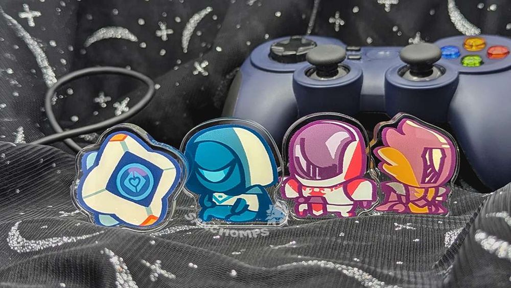 A four piece set of thick acrylic standees. From left to right, there is the Ghost, Hunter, Titan and Warlock from Destiny 2. They are against a backdrop of a stars and moon glitter fabric and a game console controller.