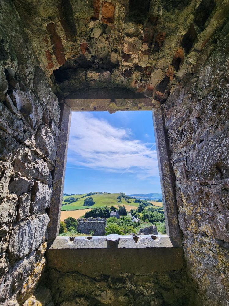 View out a castle window at the ruinous lower castle nestled in green hills and blue sky