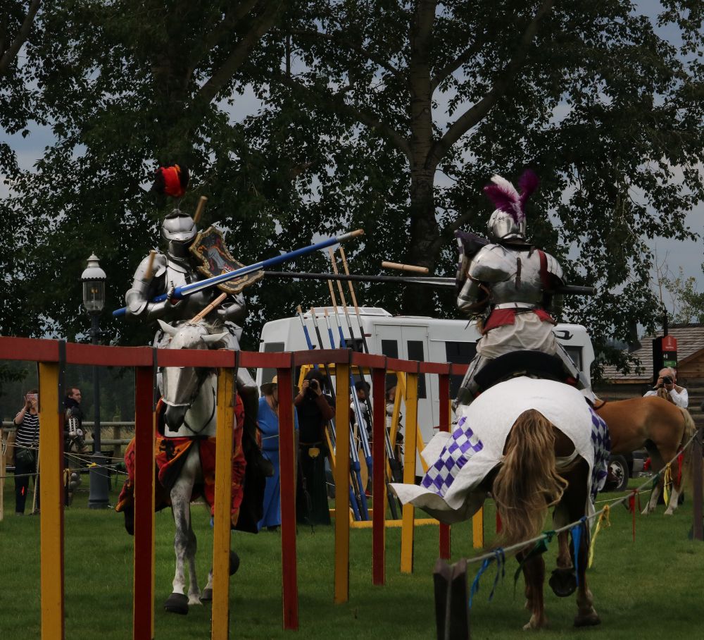 Two knights charge head on with their lances connecting. The red knight scores over the purple knight. 