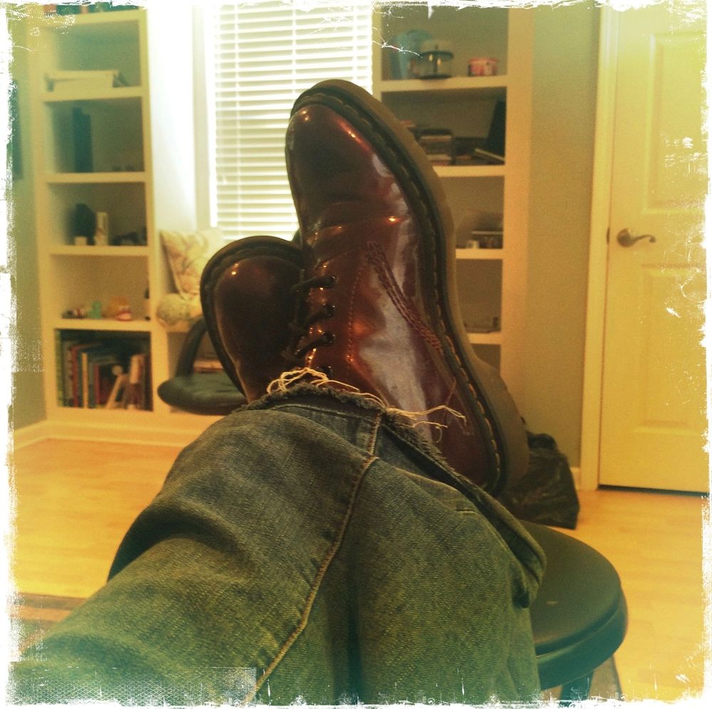 a person wearing a pair of red shiny boots propped up on a stool.