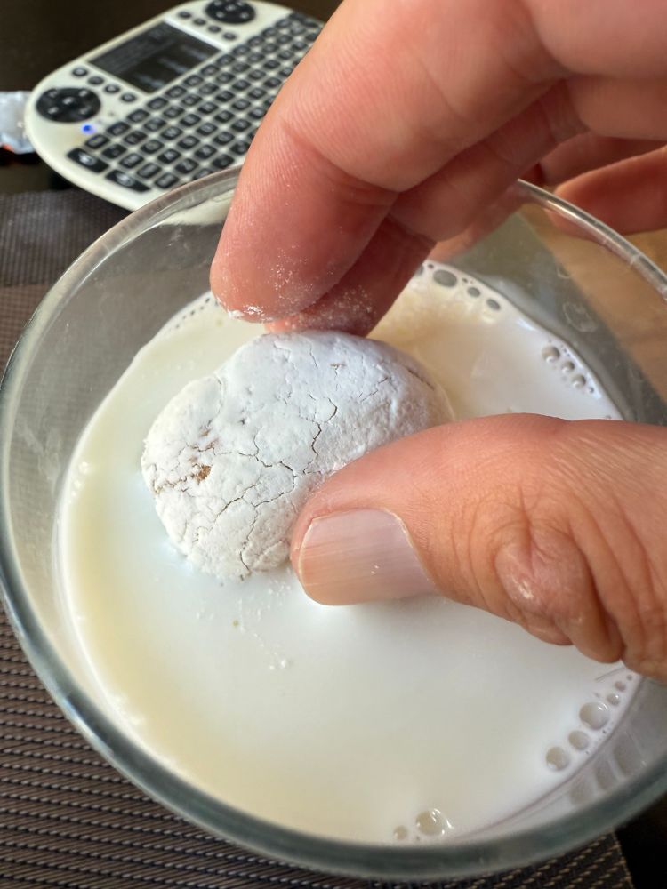 hand dunking powdered donut in milk