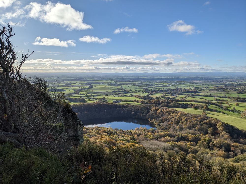 View of a lake looking down from a hill onto the woodland below on a sunny day.