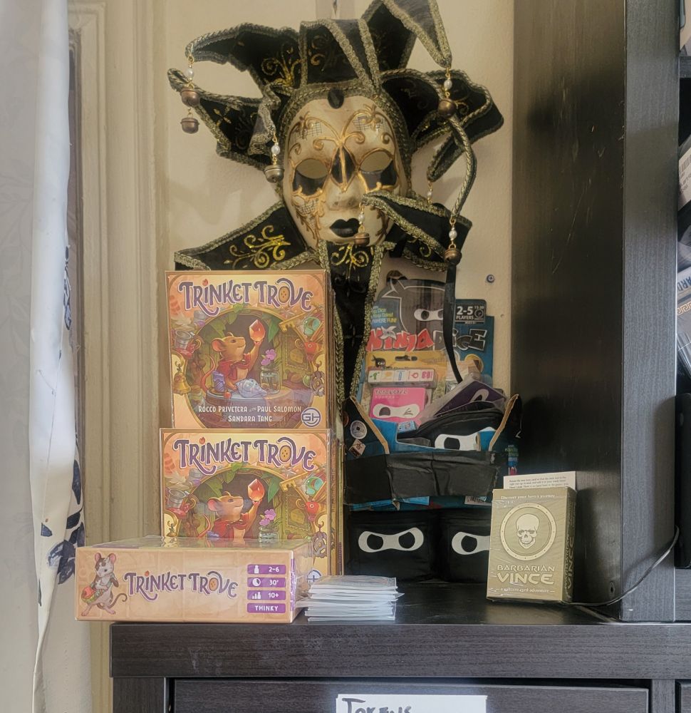 A shelf with boardgames, including Trinket Trove, Ninja Dice, and Barbarian Vince.