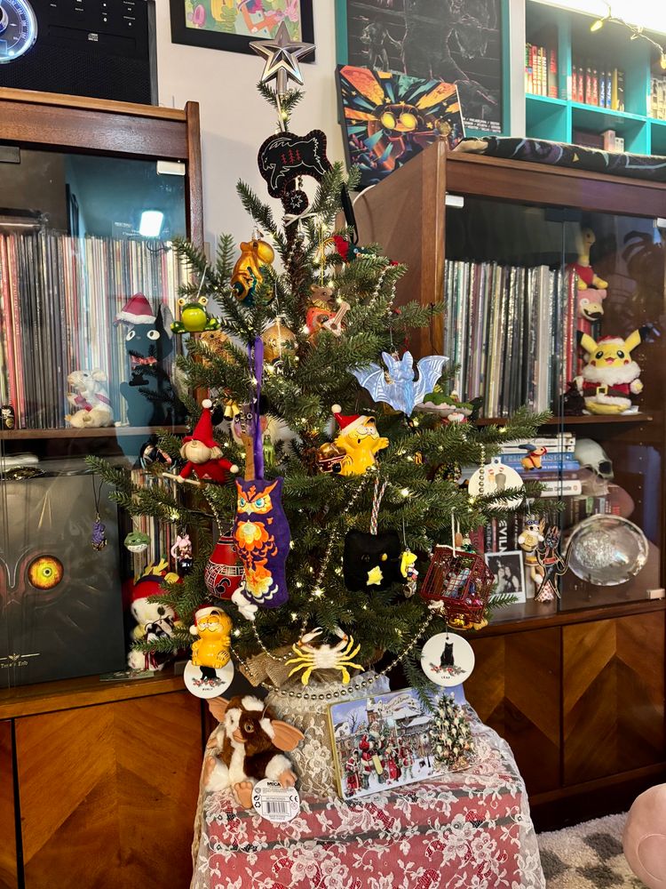 a small (3 ft?) fake xmas tree that’s covered in ornaments that are frankly too big for it, sitting between two record cabinets 