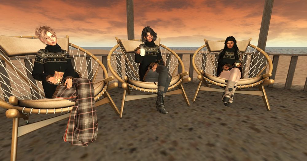 Three female avatars sitting around a campfire, each with a different drink in their hand. They are all wearing hte same poncho-style top with a turtle-neck top, with different complementary outfits. 