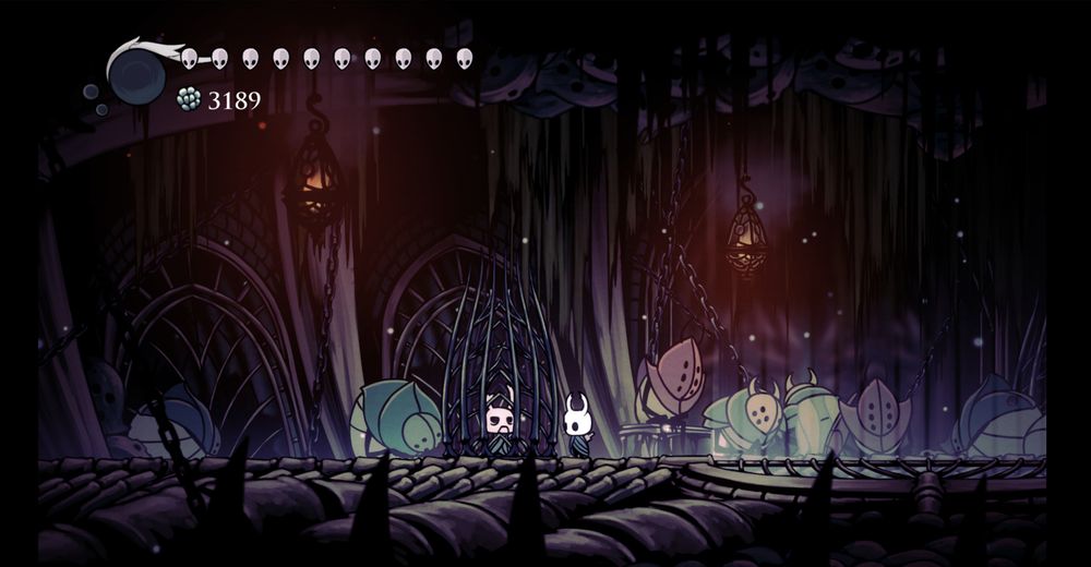 Зображено скріншот гри Hollow Knight: Ми можемо бачити, що у гравйця нема душ, але 3189 гео та 10 повних маск. Локація, похмура роздягальня для учасників Колізея Дурнів, на фоні видно багато втомлених дурнів, які завмерли в різних позах. В центрі - клітка з Могутнім Зотом, неігровим персонажем, в якого майже повністью відсутня бойова міць, але максимально сильно розвинене его та гіпертрафована самооцінка. Поруч з ним стоїть наш ігровий персонаж 