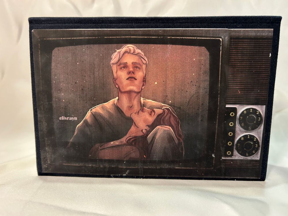 Back Cover of The Fallout fanfic bind on its side to look like an old school TV set with an image of Hermione laying on Draco’s lap and both of them looking up to the stars. 
