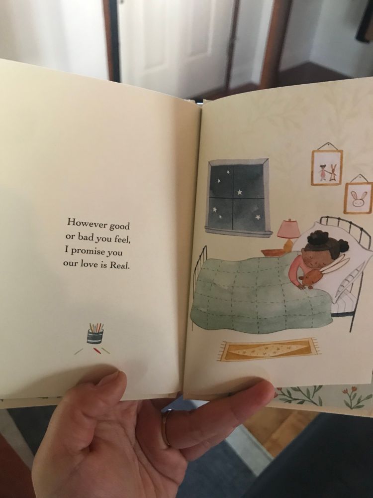 Two pages from a children’s book. The first page includes text: “However good or bad you feel, I promise you our love is Real”. The next page shows a storybook illustration black girl with space buns cuddling a brown bunny stuffy in her bed.