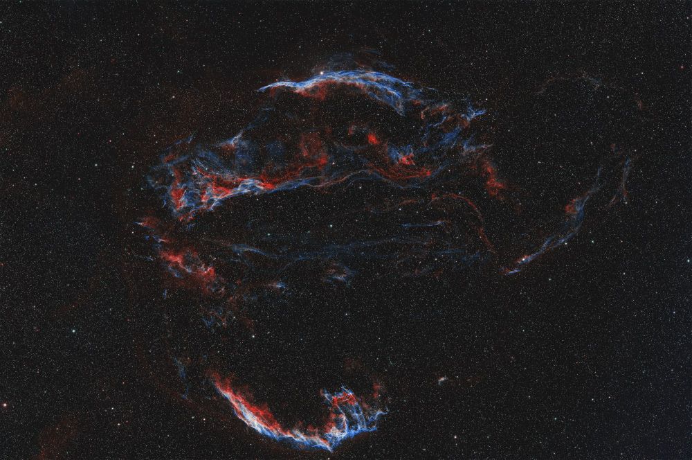 Several nebula come together to form loops and swirls of gas, glowing red and blue amongst a blanket of stars. 