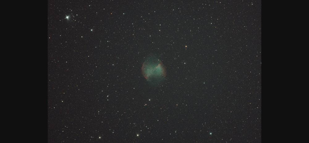 The dumbbell nebula is faintly visible with stars around it 