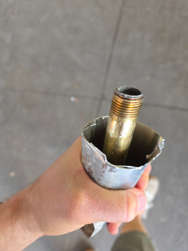A bathtub downspout hacksawed in half with a stuck copper pipe protruding in the grip of an overconfident man 