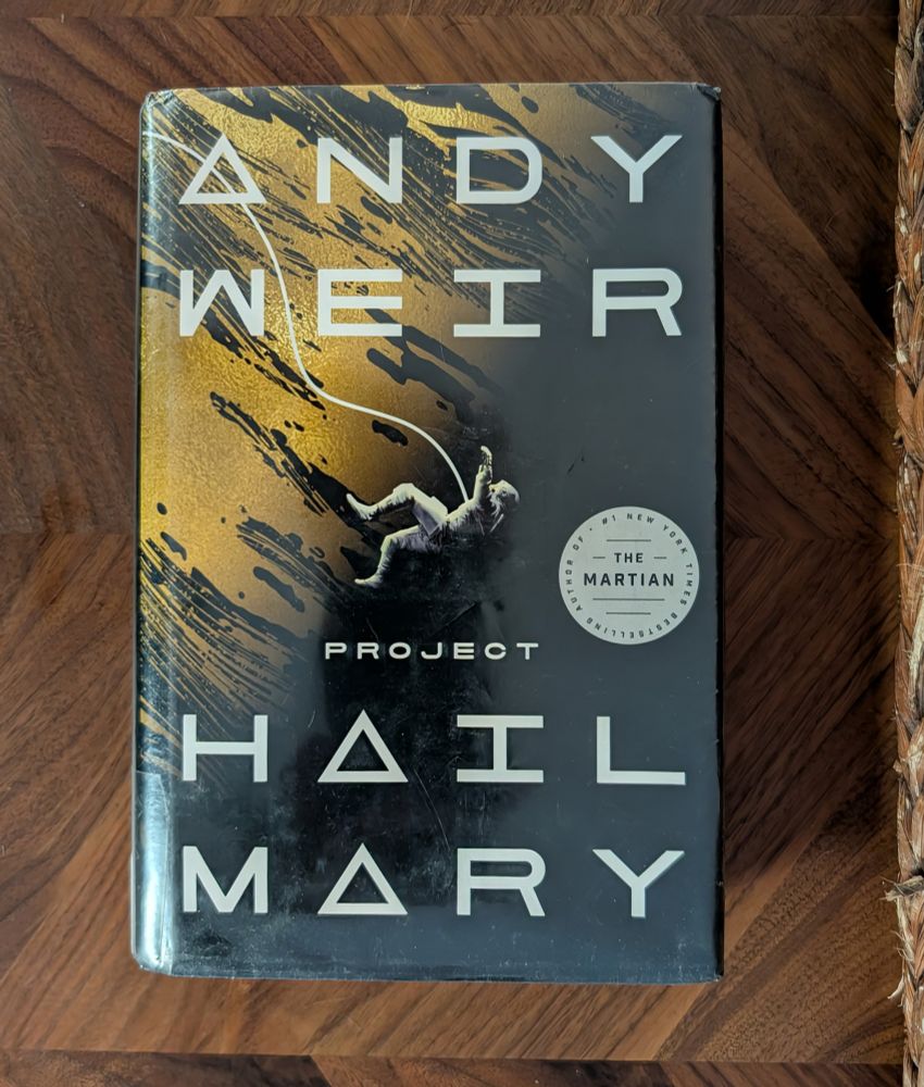 Sitting on a brown table is the science-fiction novel Project Hail Mary by Andy Weir. 