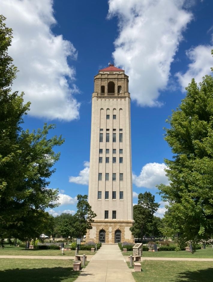 A Romanesque style tower, surrounded by trees with a blue sky and a few puffy clouds.