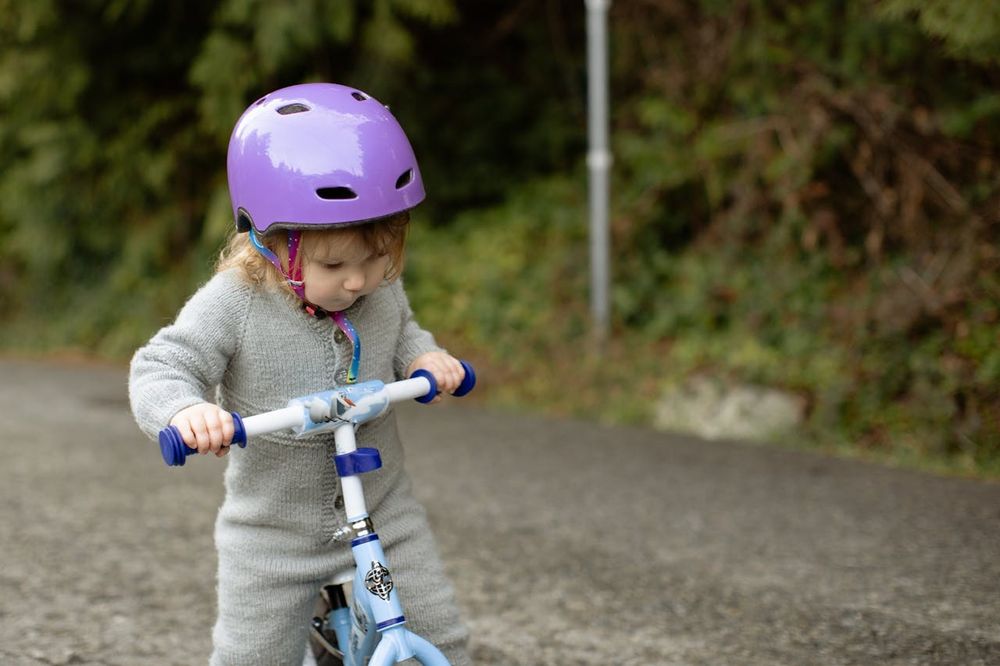 A young girl wearing a purple helmet rides a small scooter