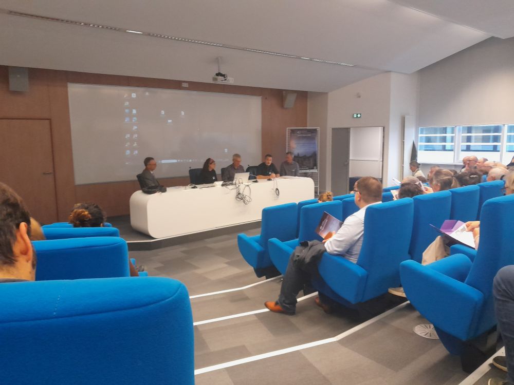 Amphi de la maison de la recherche de l'université de Toulouse. Cinq personnes à la tribune et le public dans des fauteuil bleu qui semblent confortables. 