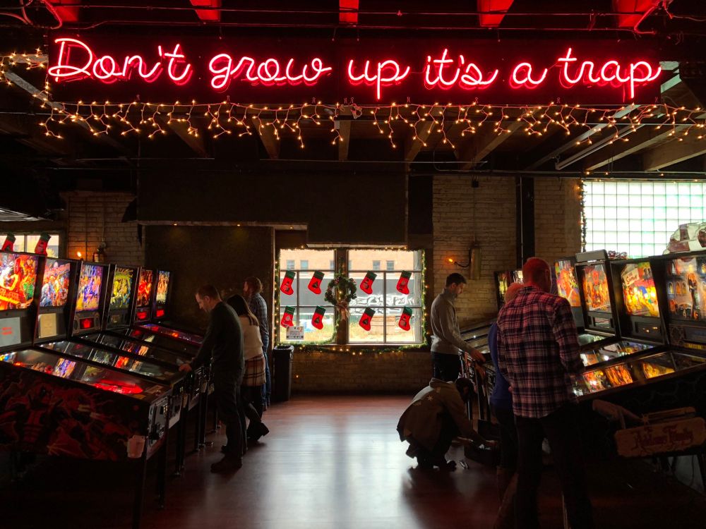 Pinball arcade with neon sign "Don't Grow Up It's a Trap"