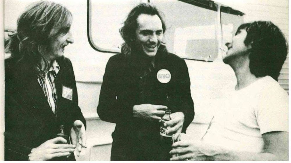 Black and white photo of, from left to right, Soeedy Keen, Terence Stamp, and Keith Moon, standing in front of what appears to be a caravan/trailer in the outdoor backstage area at Le Fête d’Humanitie.