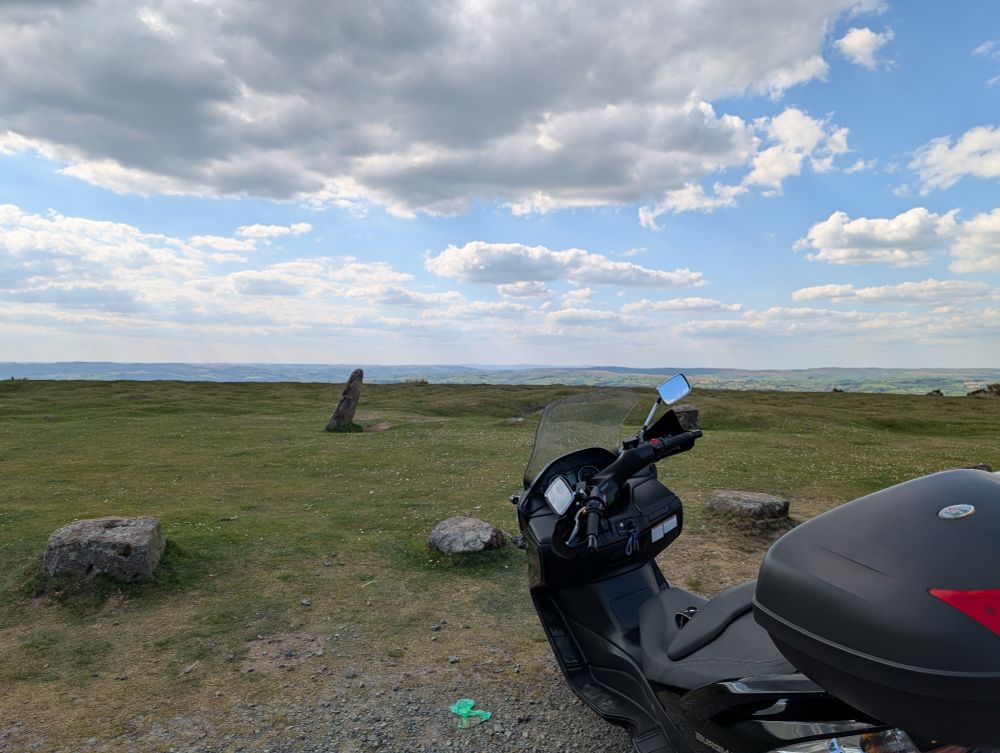 Photo of a Welsh landscape from Gospel Pass. It is a sunny day with blue skies and moderate cloud cover. There is a black scooter in the bottom right of the photo