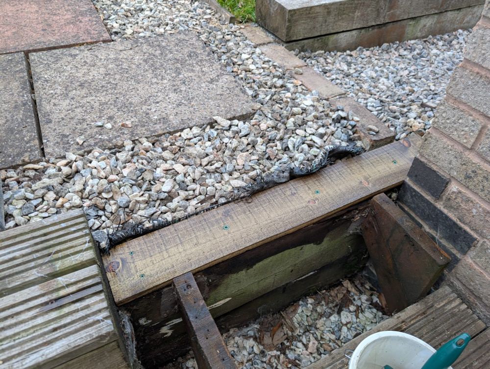 A photo of a plank of wood sitting on top of a wooden sleeper. The plank forms the top of a wooden set of stairs, with the top set of stairs missing.