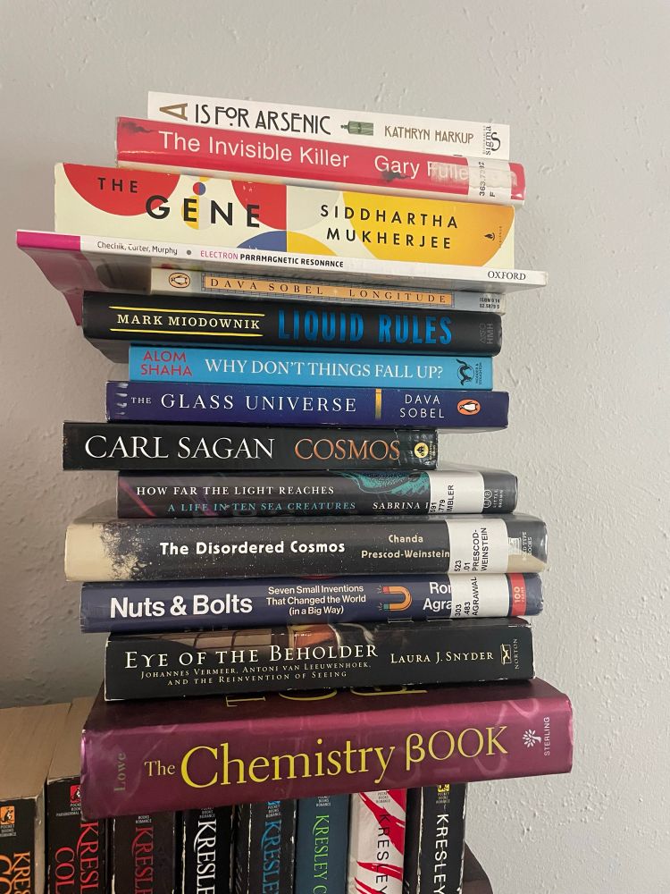 A stack of books from bottom to top:

THE CHEMISTRY BOOK by Derek Lowe
EYE OF THE BEHOLDER by Snyder
NUTS AND BOLTS by Roma Agrawal
THE DISORDERED COSMOS by Chanda Prescott’s-Weinstein 
HOW FAR THE LIGHT REACHES
COSMOS
THE GLASS UNIVERSE
WHY DONT THINGS FALL UP?
LIQUID RULES
LONGITUDE 
THE GENE 
THE INVISIBLE KILLER
A IS FOR ARSENIC 