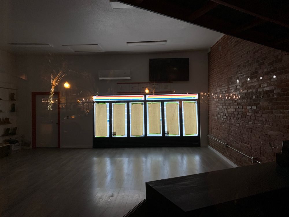 An empty store front at night. The soda coolers have brown Kraft paper taped over their windows. 