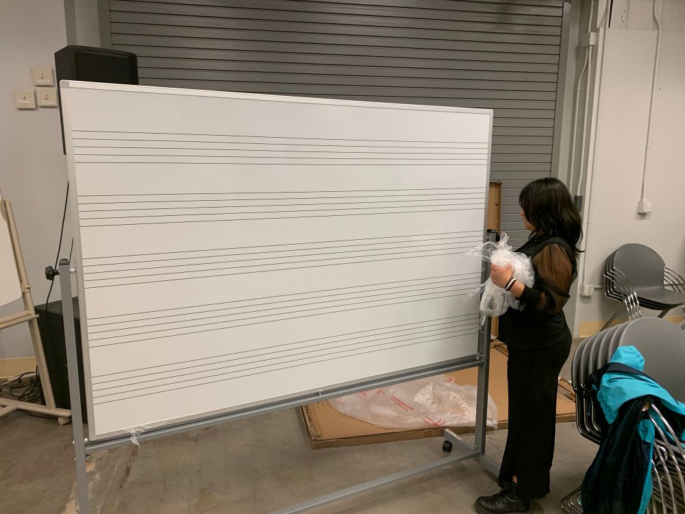 A young woman who has just finished putting together a whiteboard finishes peeling off the protective plastic layer. 