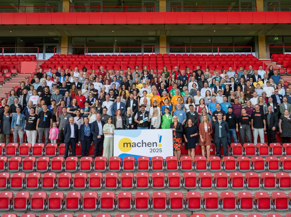 Viele Menschen stehen im Stadion an der alten Försterei auf der Tribüne mit einem Schild, auf dem steht machen 2025
