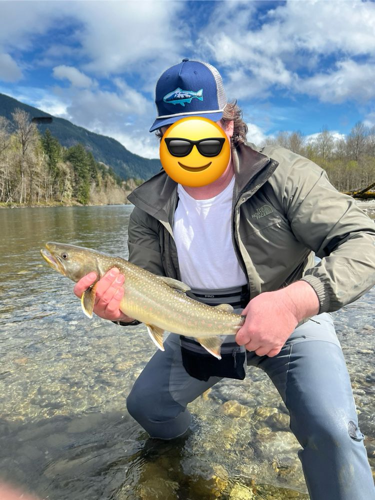 A strikingly handsome man standing in the river holding a strikingly handsome 22” bull trout freshly caught using a 7wt 12’ Spey cast rod and a black and silver #8 streamer 