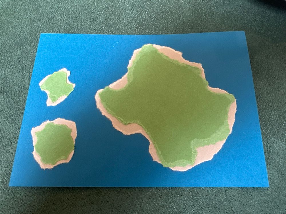 A map of 3 islands made of torn card on a blue postcard 