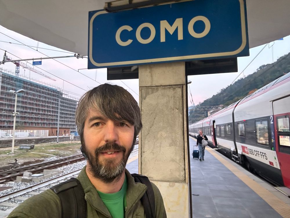 Photo of me on a train platform in front of a large blue sign saying COMO