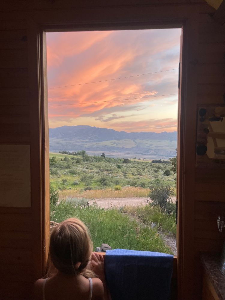 Five year old looks out a window at sunset over a mountain valley