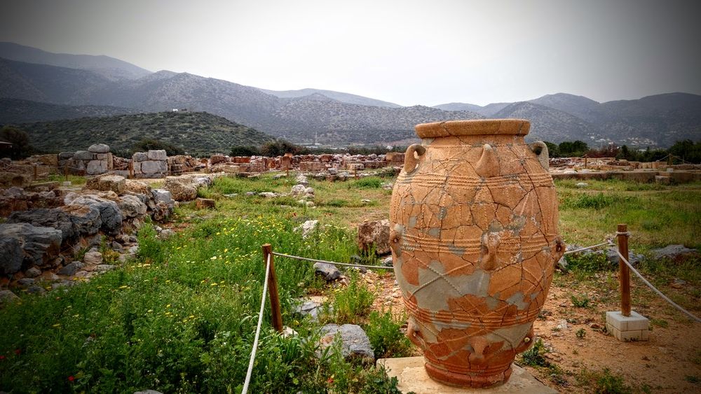 Auf einer Fläche, die teils mit Gras bewachsen ist, steht eine große Amphore von fast 2m Höhe. Auf der Fläche erkennt man Fundamente und Mauerrest eines Palastes und kleinen Stadt. Auch die Amphore scheint aus Scherben zusammengeklebt worden sein. 