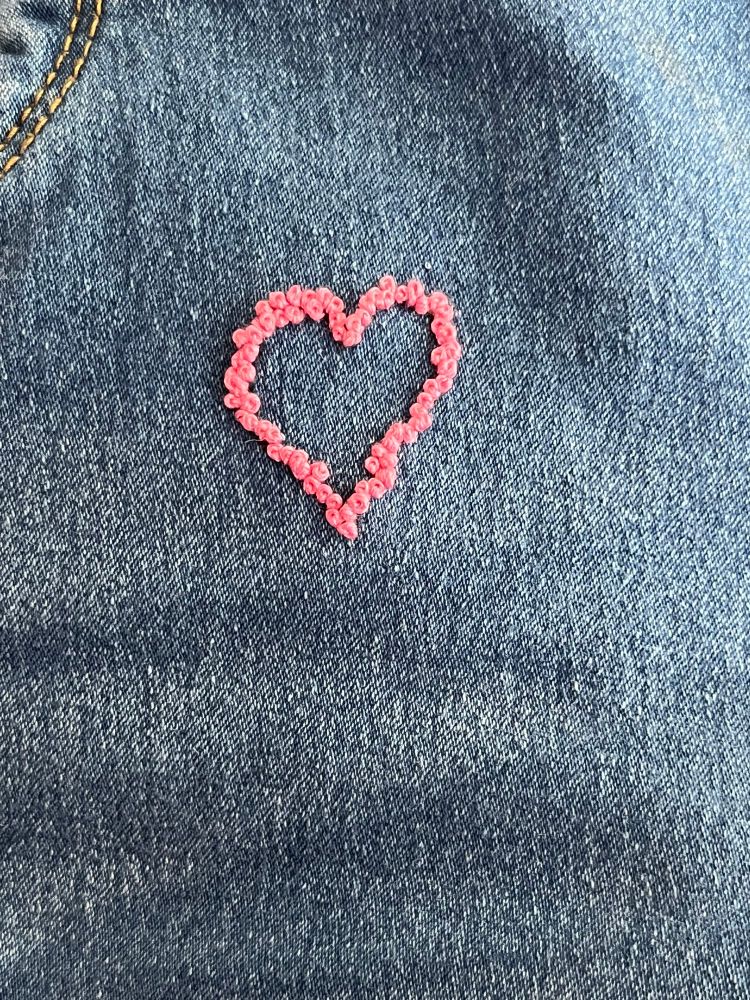 A light pink French knot heart styled to look like a wreath of roses. 