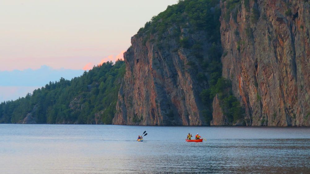 Two kayaks paddling below the towering cliffs of Bon Echo Provincial Park in Ontario.