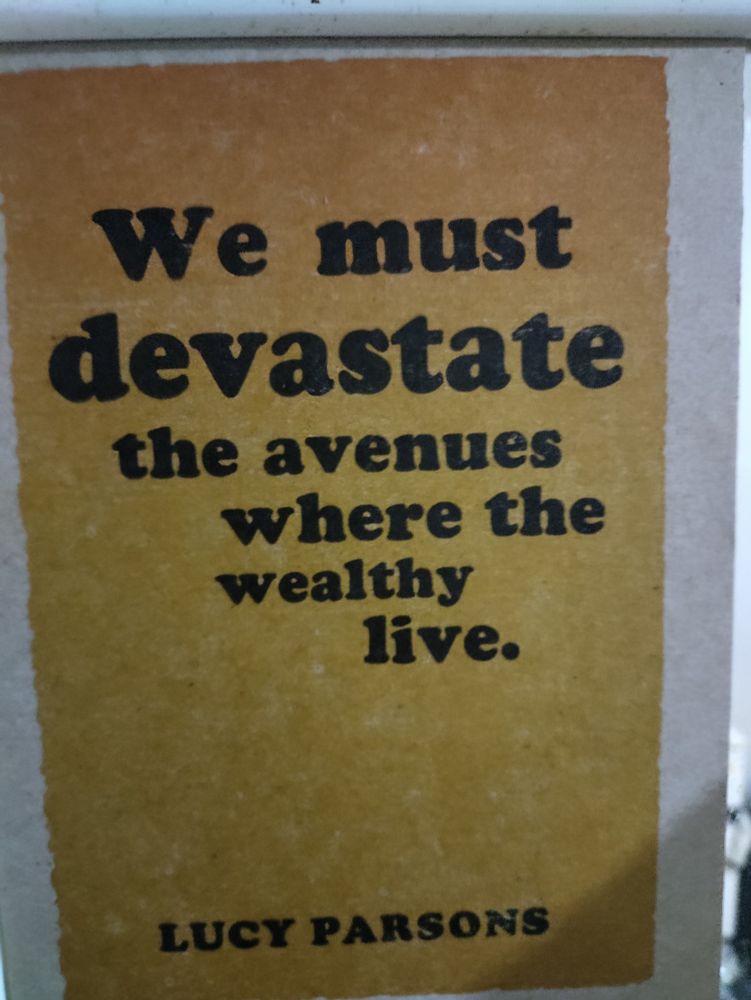 small chipboard print with a yellow/orange background. In black letters the following quote lays on top: "We must devastate the avenues where the wealthy live" --Lucy Parsons