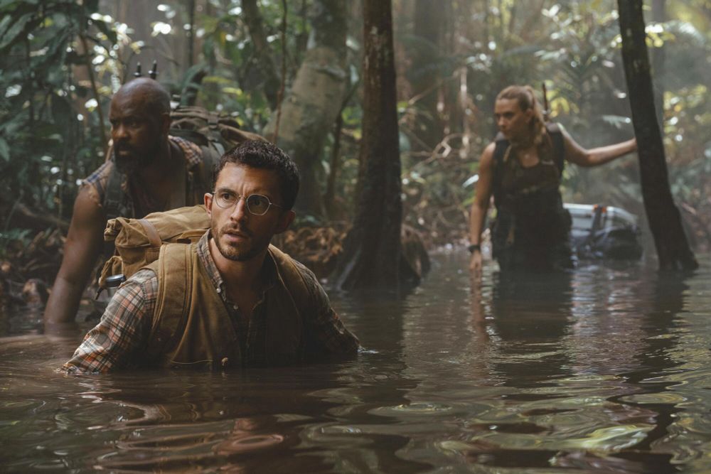 Two men and a woman walking waist deep in water in the middle of a jungle 