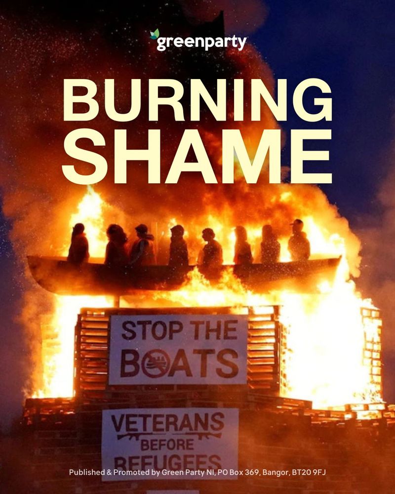 A group of life-sized dummies, posed as refugees in orange life jackets, are packed into a small boat placed on top of a tall bonfire built from wooden pallets. Large banners reading “STOP THE BOATS” and “VETERANS BEFORE REFUGEES” are attached to the bonfire. The Green Party logo is visible at the top, and bold text reads “BURNING SHAME.” The scene is outdoors at night, with the bonfire ablaze, creating an atmosphere of hostility and intimidation. No real people are present.