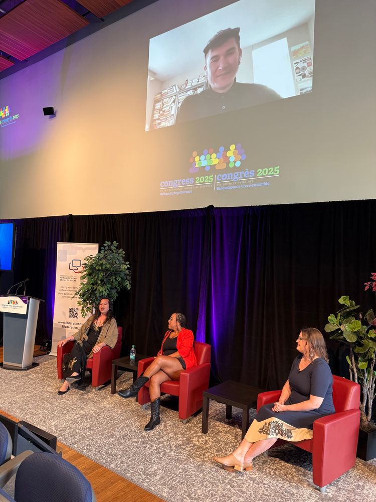 Kai Cheng Thom, Jael Richardson, and Kisha Supernant sit in red chairs and above on the wall is the projected image of Billy Ray Belcourt participating online in the Big Thinking panel Care of Togetherness 