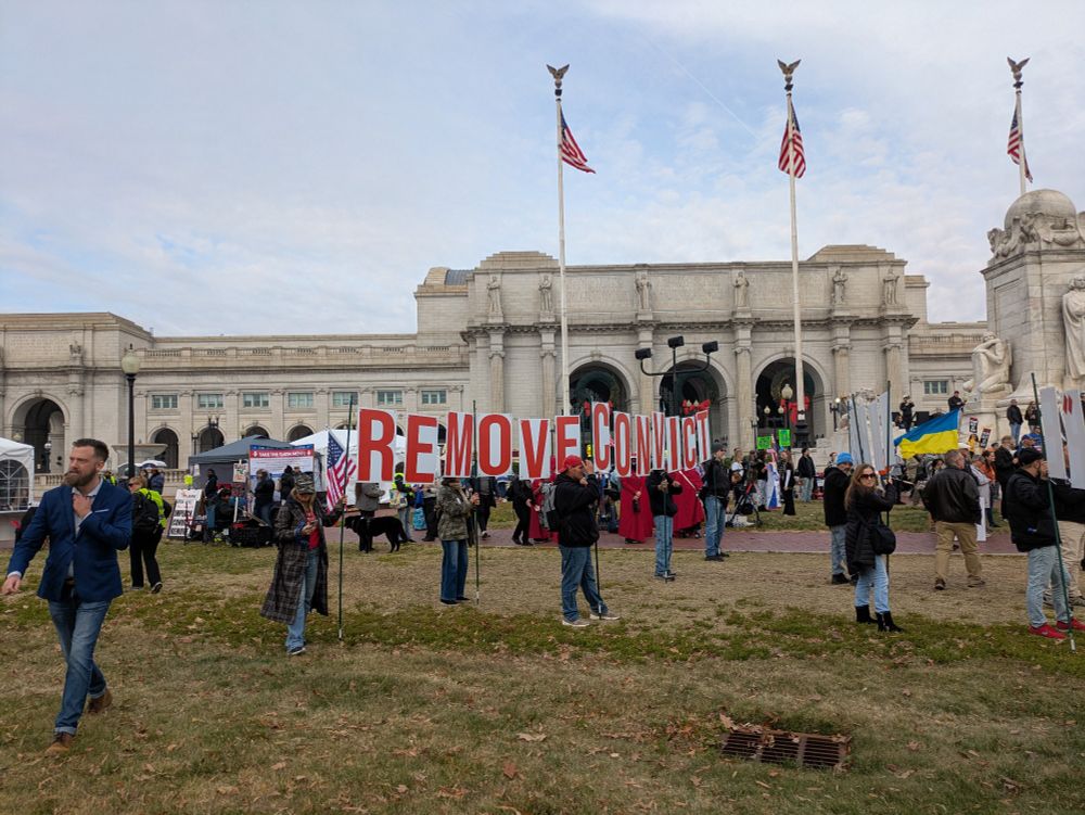 A protest outside with a large sign that reads "impeach, convict, remove"