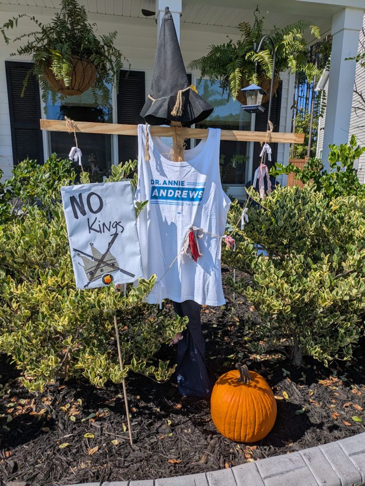 A scarecrow dressed in a tee shirt that reads "Dr. Annie Andrews for Senate" there is a pumpkin on the ground and a "No Kings" sign