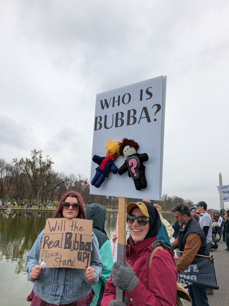 Two people holding signs that read "who is bubba?" and "will the real bubba please stand up"