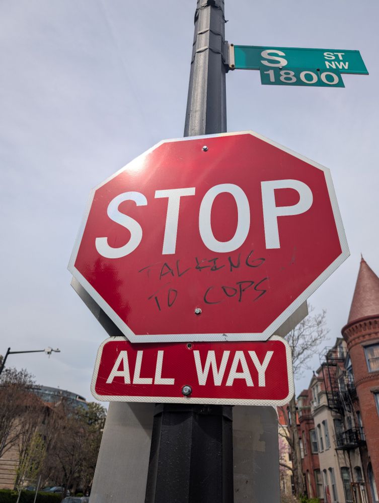 A Stop sign on the corner of the 1800 block of S Street in Washington DC. Under "Stop", the phrase "talking to cops" is written in black marker. 